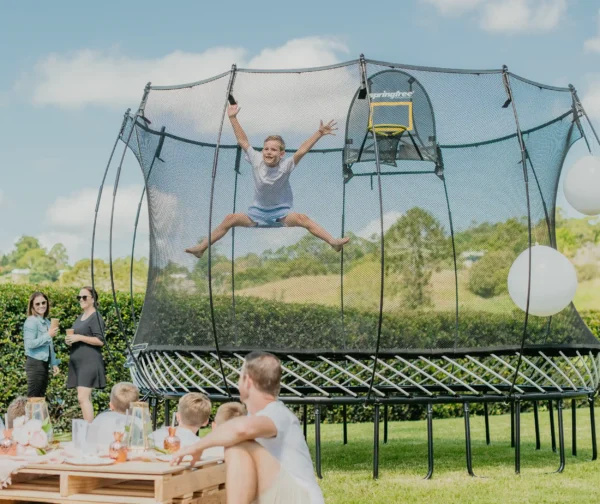 Chlapec skáče a raduje se na trampolíně Springfree a jeho rodina jej u toho sleduje